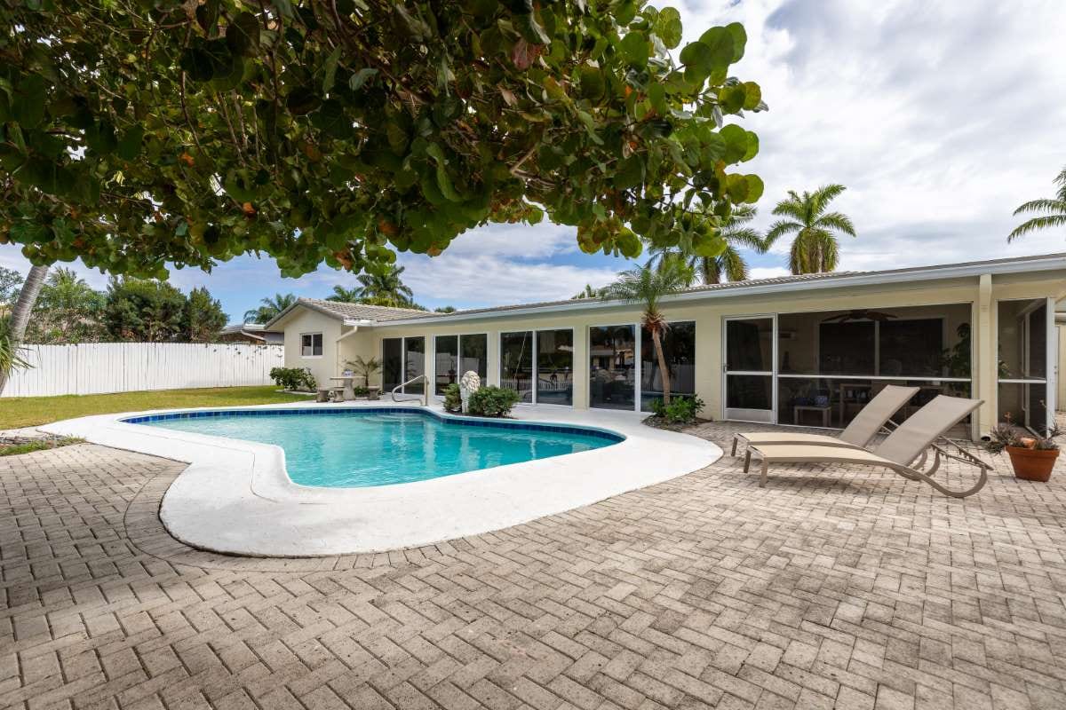 Modern backyard with swimming pool, stone path, patio chairs, and trees