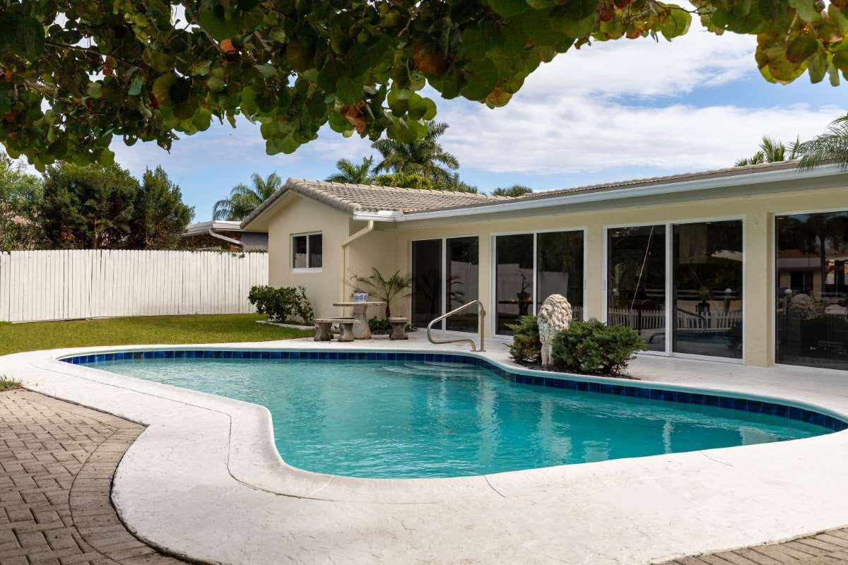 Modern backyard with swimming pool, stone path, artificial grass, trees and lounge chairs
