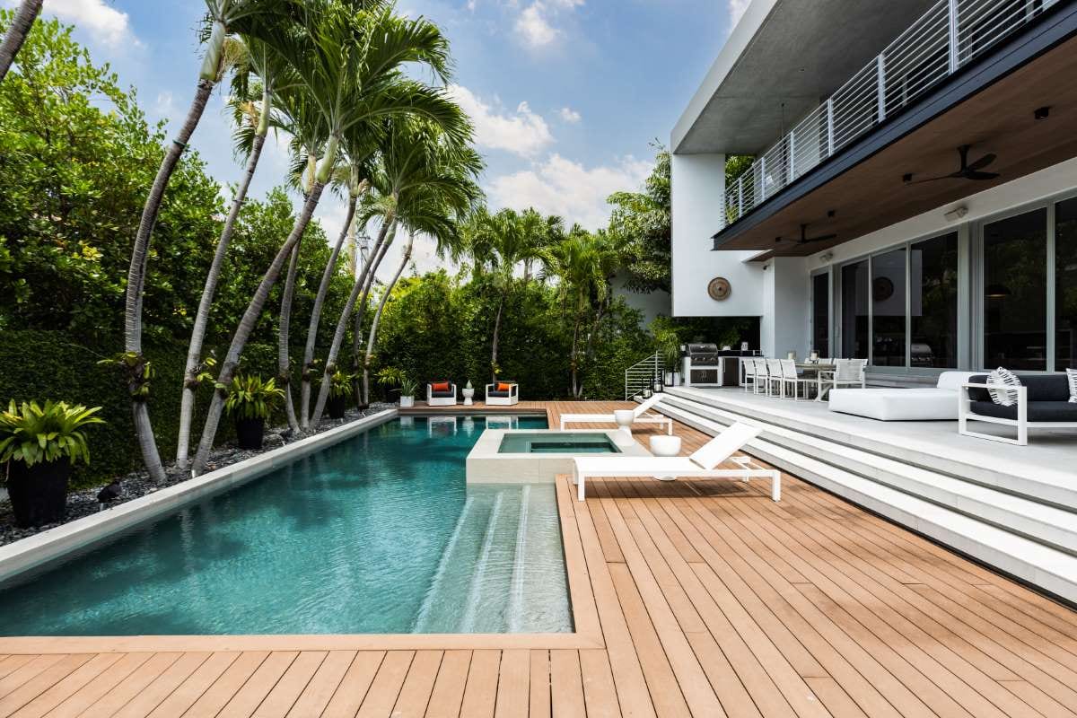 Modern backyard with swimming pool, artificial grass, stone path, trees, and chairs