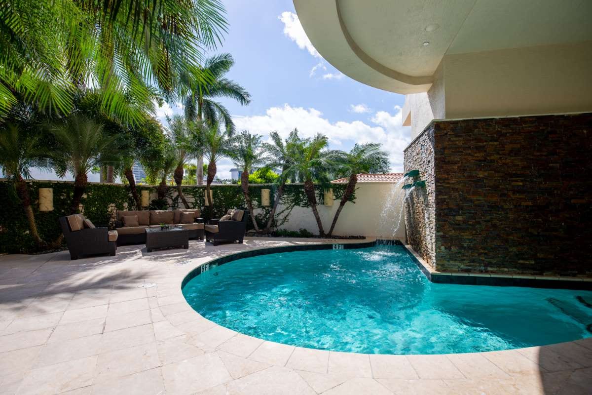 Modern backyard with pool, artificial grass, stone path, trees, and chairs