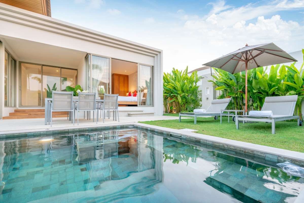 Tropical pool villa exterior with greenery, sunbeds, umbrella, and pool towels