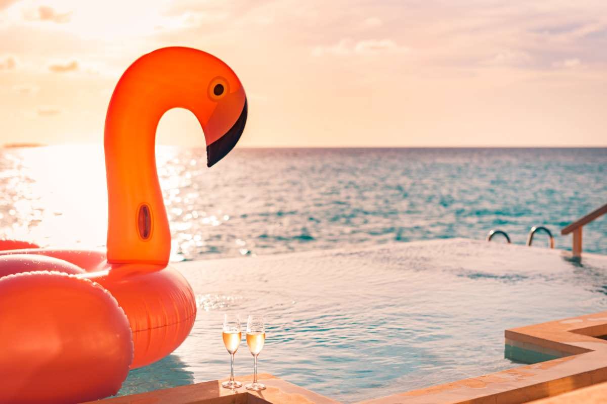 Couple by a luxury infinity pool at sunset with a flamingo float and drinks