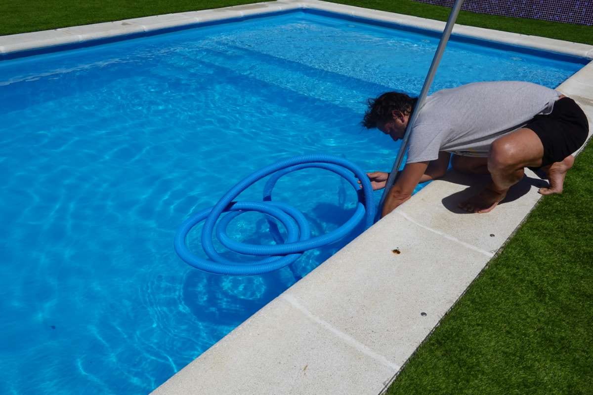 Man connecting a pool cleaner pipe beside a swimming pool
