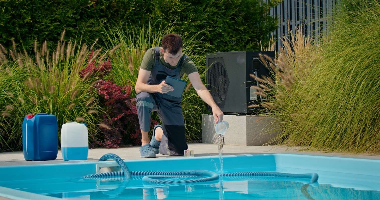 Pool technician pouring liquid into a pool while checking a tablet beside chemical containers