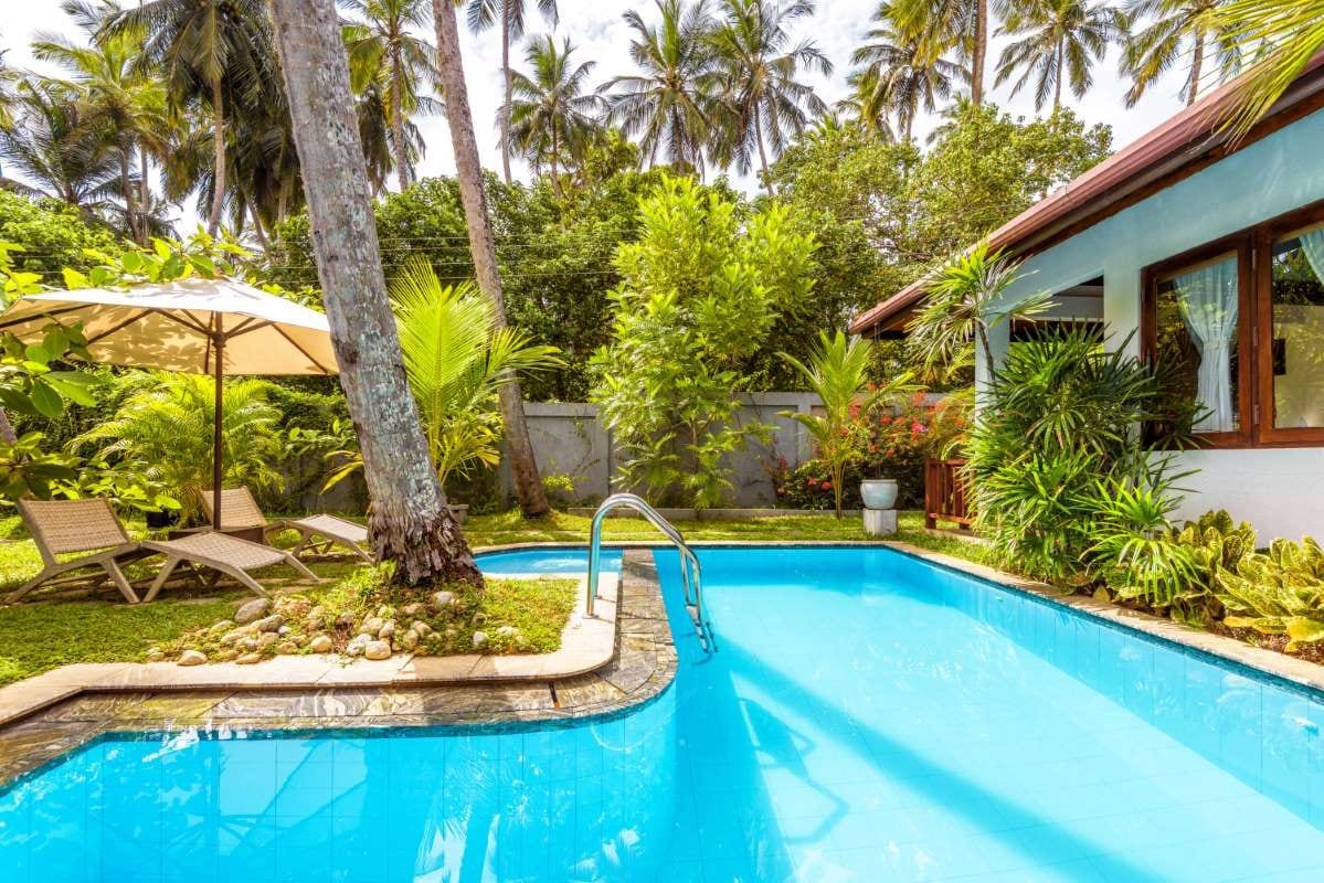 Tropical hotel pool with umbrella and beach beds in a backyard setting