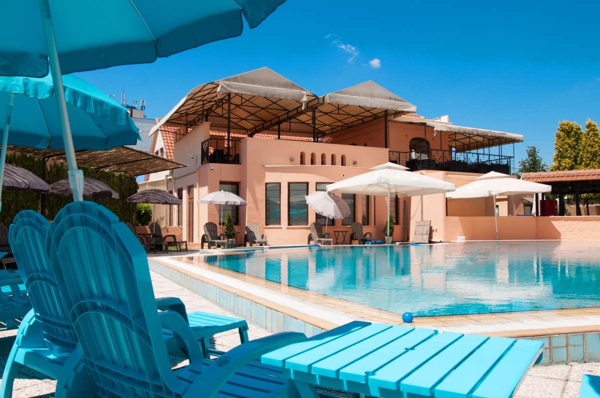 Umbrella, poolside chairs, and a building beside water under a clear blue sky