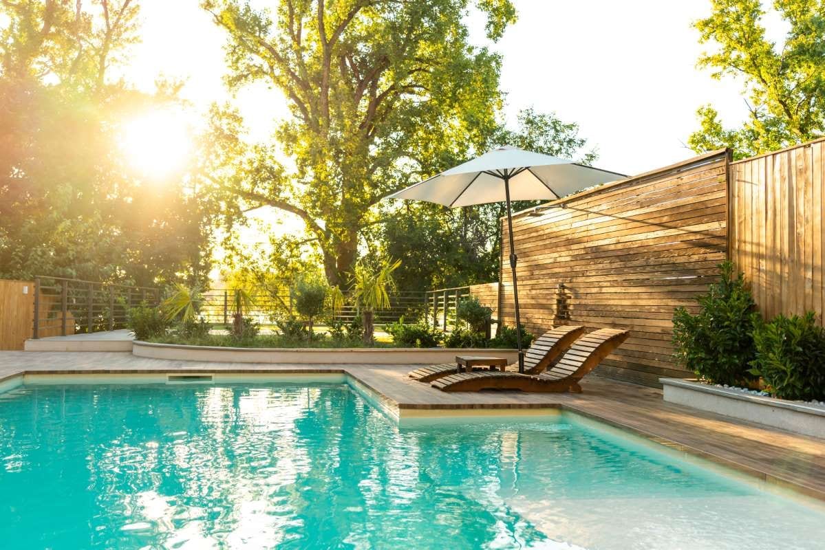 Modern private villa pool with lounge chairs, palm trees, and umbrella by the water